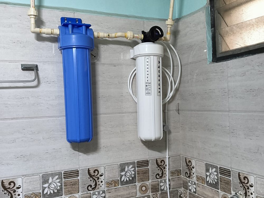 Dual-stage water filter housing mounted on bathroom wall